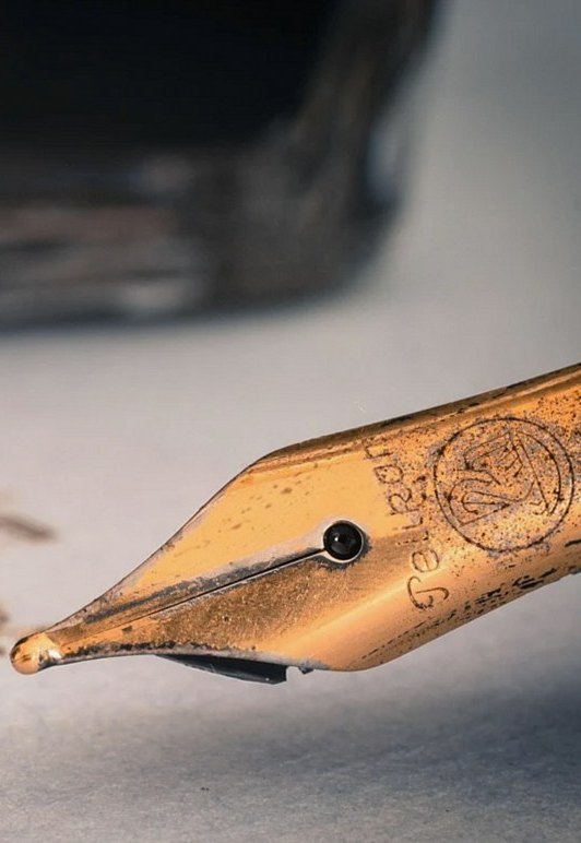 インク瓶の手前で、万年筆のペン先が紙に触れている接写（イメージ写真）